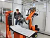 Kuka-Mitarbeiter steht vor Roboterzelle und schaut auf ein Tablet.