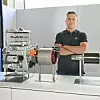 Mathias Miedreich, ZF-Vorstandsmitglied für Elektrifizierte Antriebstechnologien, steht mit verschränkten Armen hinter einer Ausstellung von Komponenten der Select-Plattform. Zu sehen sind unter anderem E-Motor, Inverter, Reduziergetriebe und weitere Elemente des modularen E-Antriebssystems. Im Hintergrund das ZF-Logo und ein Monitor mit technischer Explosionsgrafik.