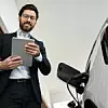 Mann mit Tablet steht neben einem Elektroauto