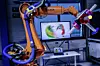 Ein Kuka-Roboter bei Volkswagen im Einsatz, im Hintergrund ein aufgeklappter Laptop.