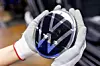 Mitarbeiterin in der Montage hält ein VW-Emblem