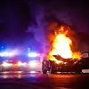 Ein brennendes Auto auf der Straße steht vor zwei Polizeiautos mit blinkender Sirene.