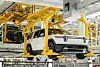 Weißes Rivian-Elektroauto hängt in gelber Förderanlage einer Fabrikhalle