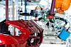 Ein orangefarbener Industrieroboter prüft mit einem Terahertz-Messkopf die Lackschicht eines rot lackierten Kunststoffaußenhautteils in der Fertigung.
