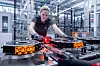 Eine Mitarbeiterin von Mercedes-Benz prüft in einer hellen Produktionshalle Bauteile eines elektrischen Axial-Fluss-Motors. Im Vordergrund sind scheibenförmige Motorkomponenten auf einer Fertigungsanlage zu sehen, während rote Sensorsignale den Prüfvorgang markieren.