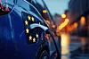 KI-generierte Nahaufnahme eines blauen Elektroautos an einer Ladestation. Der Ladestecker steckt in der seitlichen Ladebuchse, die von gelben Sternen als Symbol für die Europäische Union umgeben ist. Blaue Fahrzeugflächen und warme Lichtreflexe im Hintergrund verweisen auf Elektromobilität und den europäischen Markt.