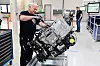 Alt-Text:
Ein Mitarbeiter montiert mit einem Akkuschrauber ein Brennstoffzellensystem in einer hellen Produktionshalle. Im Hintergrund arbeitet ein weiterer Beschäftigter an einer Anlage.