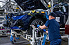 Ein Mitarbeiter montiert in einem BMW-Werk ein Vorderrad an einem blauen Fahrzeug auf der Produktionslinie.