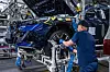 Ein Mitarbeiter montiert in einem BMW-Werk ein Vorderrad an einem blauen Fahrzeug auf der Produktionslinie.