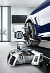 A blue BMW on a wheel alignment lift with measuring equipment in front of the tyre and a wall display behind it.