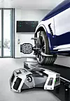 A blue BMW on a wheel alignment lift with measuring equipment in front of the tyre and a wall display behind it.