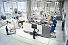 Wide view of an industrial hall with large machines, workstations and workers near a BMW additive manufacturing setup.