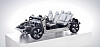 Cutaway electric vehicle platform with seats mounted on a white display stand against a plain background.