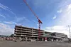 Mehrstöckiger Gebäudekomplex im Rohbau mit großem Baukran unter blauem Himmel.