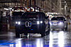 Zwei BMW X5 fahren in einer hellen Produktionshalle auf einer nassen Montagefläche.