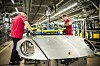 Zwei Arbeiter montieren an einer silbernen Porsche-Karosserie in einer Werkhalle.