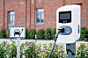 Eine öffentliche Ladesäule für Elektroautos steht vor einem Backsteingebäude neben einem Parkplatzschild.