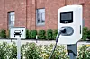 Eine öffentliche Ladesäule für Elektroautos steht vor einem Backsteingebäude neben einem Parkplatzschild.