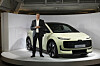 Ein Mann steht neben einem hellen Audi A2 e-tron auf einer Messebühne.