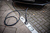 Ein Ladekabel verbindet ein Elektroauto mit einer im Bordstein integrierten Ladestation. Der Ladeanschluss ist direkt in den Boden eingelassen.