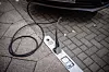 Ein Ladekabel verbindet ein Elektroauto mit einer im Bordstein integrierten Ladestation. Der Ladeanschluss ist direkt in den Boden eingelassen.