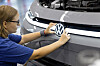 Mitarbeiterin befestigt das VW-Logo an der Front eines grauen ID.3 Neo in einer Werkhalle.