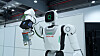 Weißer humanoider Roboter mit Greifarm in einer modernen Industriehalle.