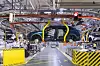 Automobilmontagehalle mit hängenden Fahrzeugkarosserien über einer Produktionslinie.