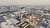 Luftbild einer großen Baustelle mit Kränen neben Industriehallen und Straßen.