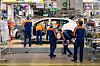 Mitarbeitende von Volvo arbeiten an einem weißen SUV auf einer Montagelinie in einem Automobilwerk.
