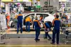 Mitarbeitende von Volvo arbeiten an einem weißen SUV auf einer Montagelinie in einem Automobilwerk.