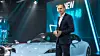 Porsche-CEO Oliver Blume steht vor einem hellblauen Porsche Taycan.