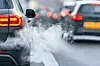 Ein Auto steht im dichten Stadtverkehr, aus dem Auspuff steigt sichtbar weißer Abgasrauch auf – Symbol für CO₂-Ausstoß und Luftverschmutzung im Straßenverkehr.