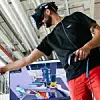 Ein Montagemitarbeiter trägt eine VR-Brille und hat einen Joystick in der Hand. Er erprobt virtuell Montageabläufe am Standort Neckarsulm